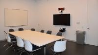 Debrief room equipped with large table, chairs, monitors, PCs, and web cameras.